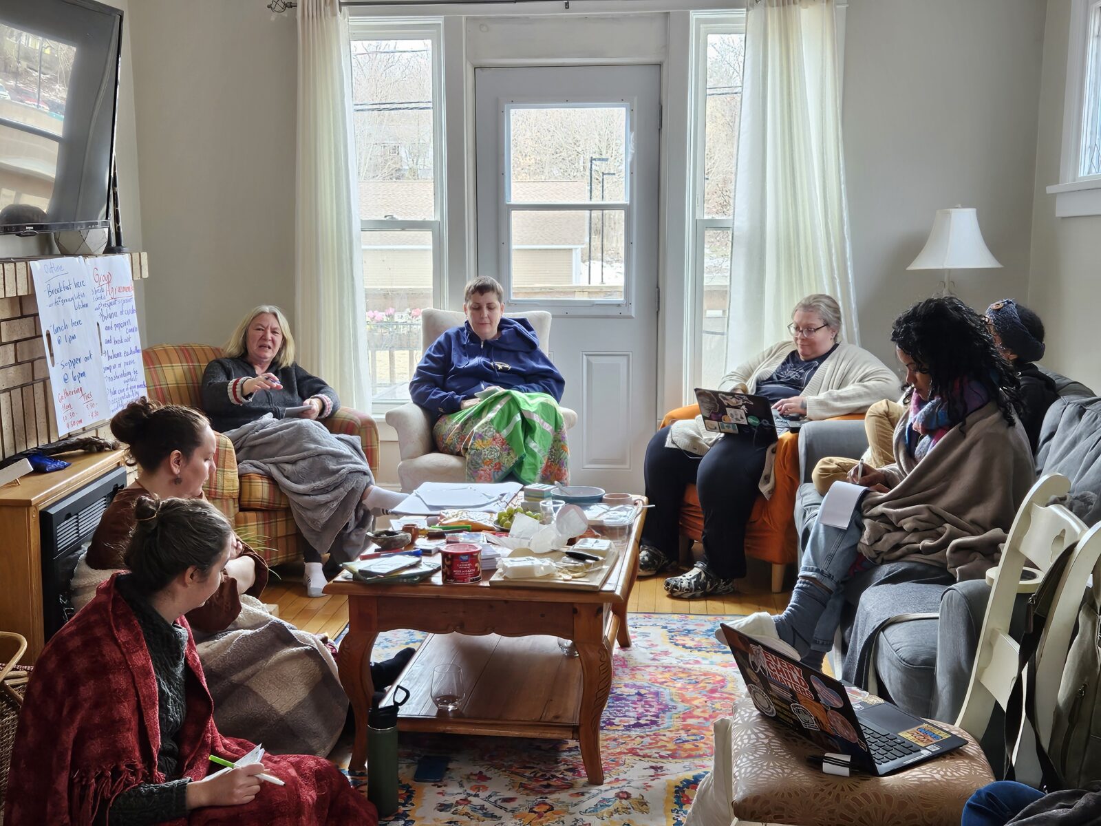 A group of women in conversation, seated in circle in a bright, cosy living room space.