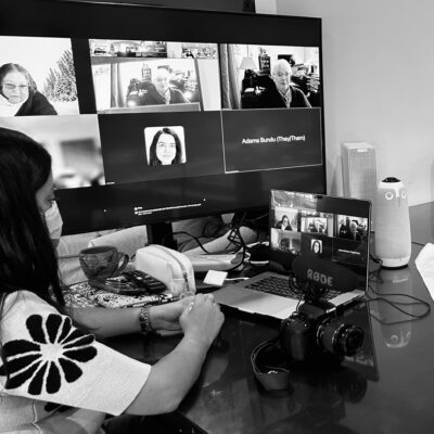 Black and white photo of a woman wearing a medical mask looking at a Zoom meeting