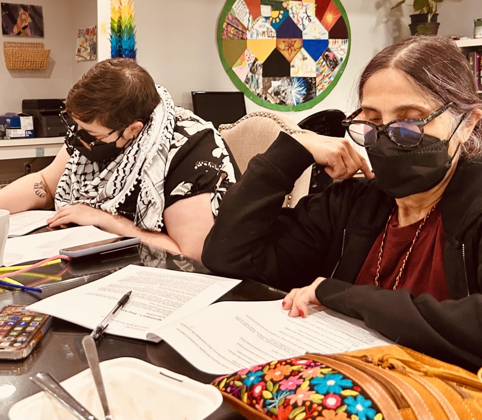 Colour photo of two women in medical masks writing at a table