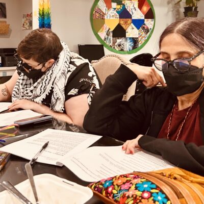 Colour photo of two women in medical masks writing at a table