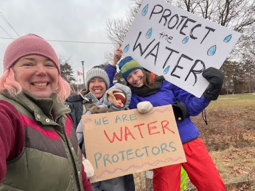 Four people pose for a selfie with 'protect the water' protest signs.