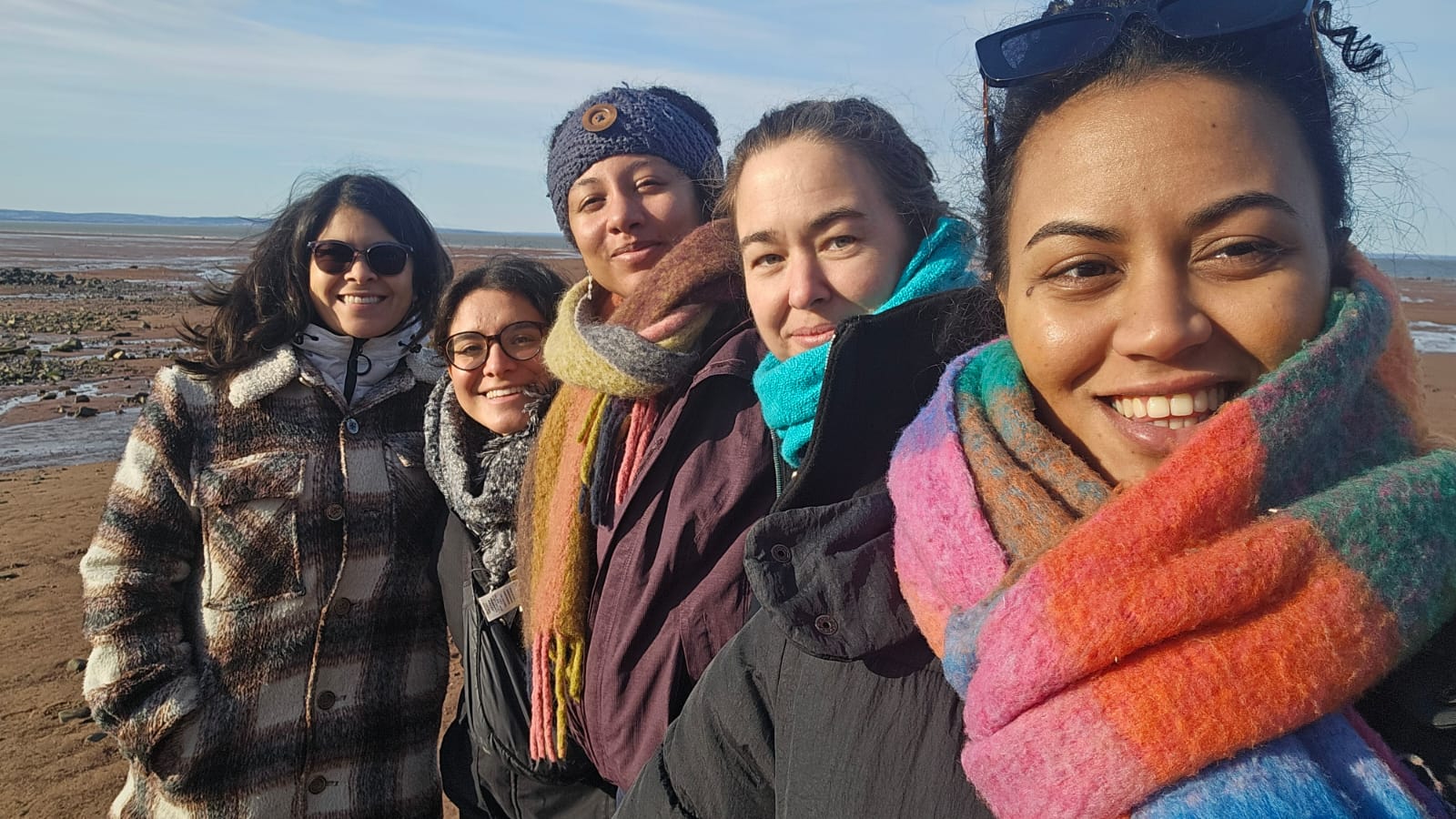 IMG-20250318-WA0004 A group of women posing for a selfie outside on a beach, wearing winter clothes
