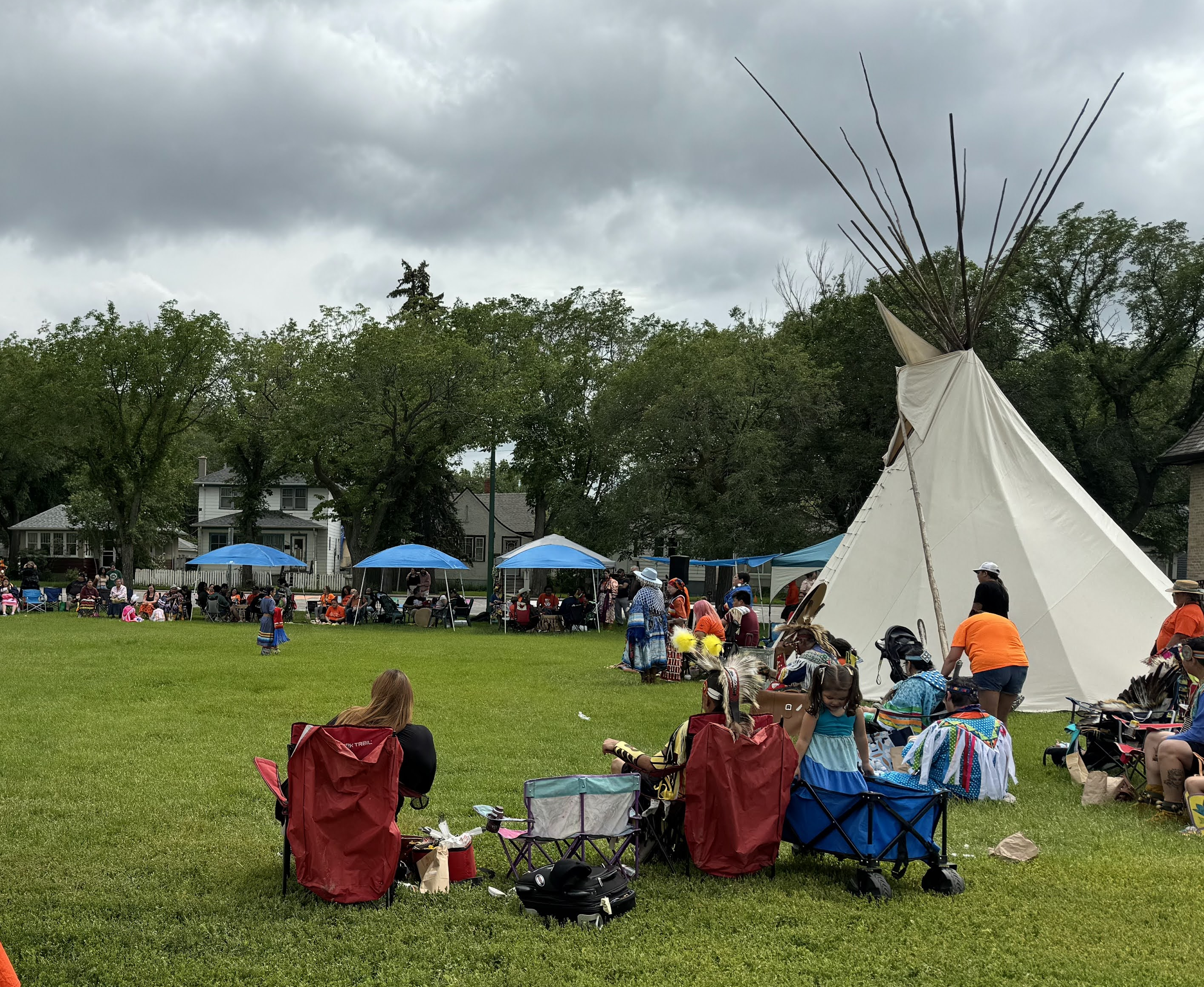 Groups of people sit in front of tents and a teepee in a field.