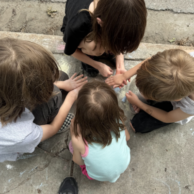 A top-down shot of four children colouring with sidewalk chalk.