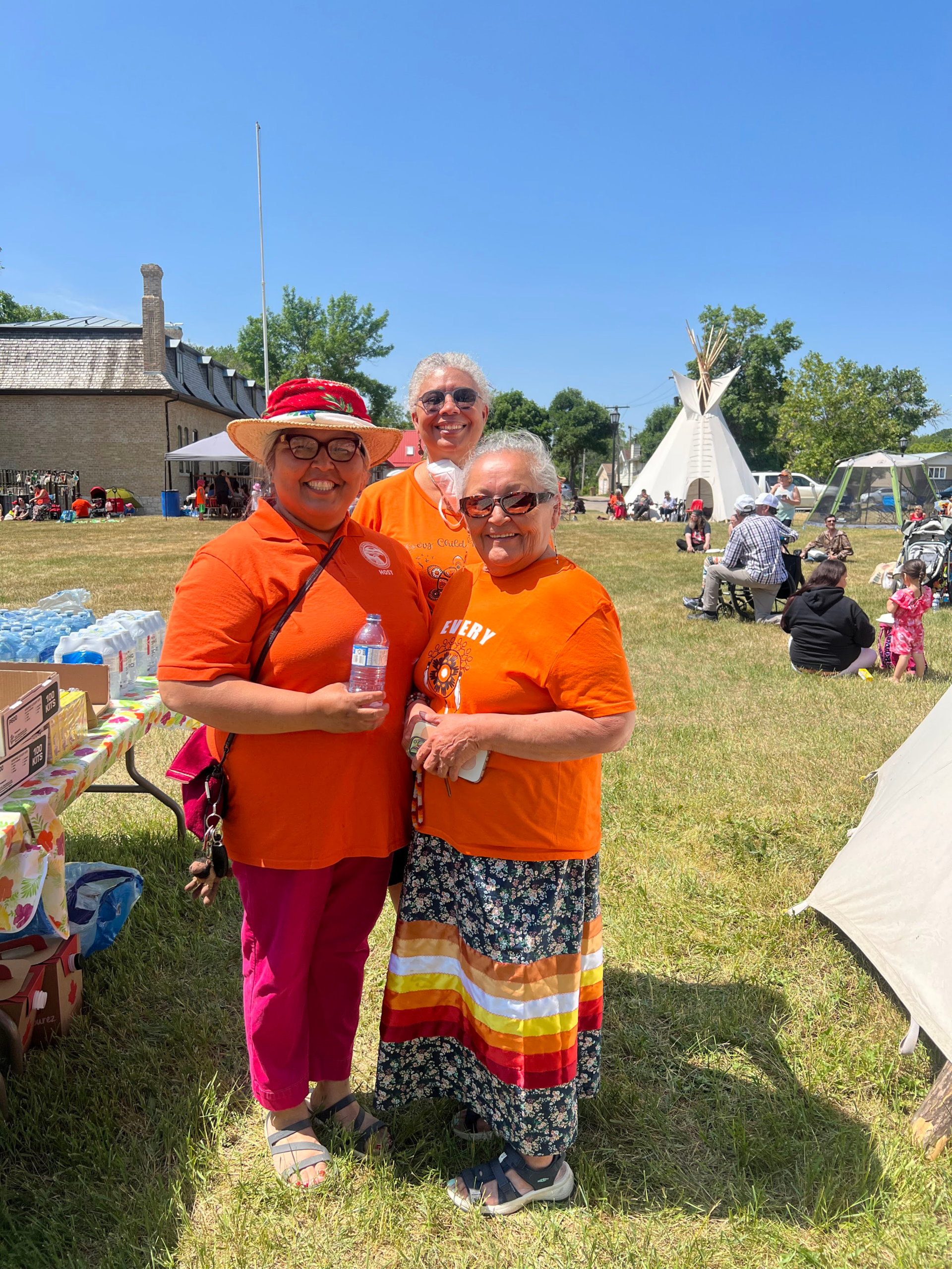 Three women in Every Child Matters shirts pose for a photo outside