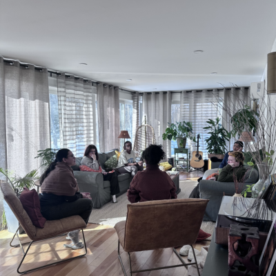 Photo of a group of young people engaged in conversation in a sunny living room space.
