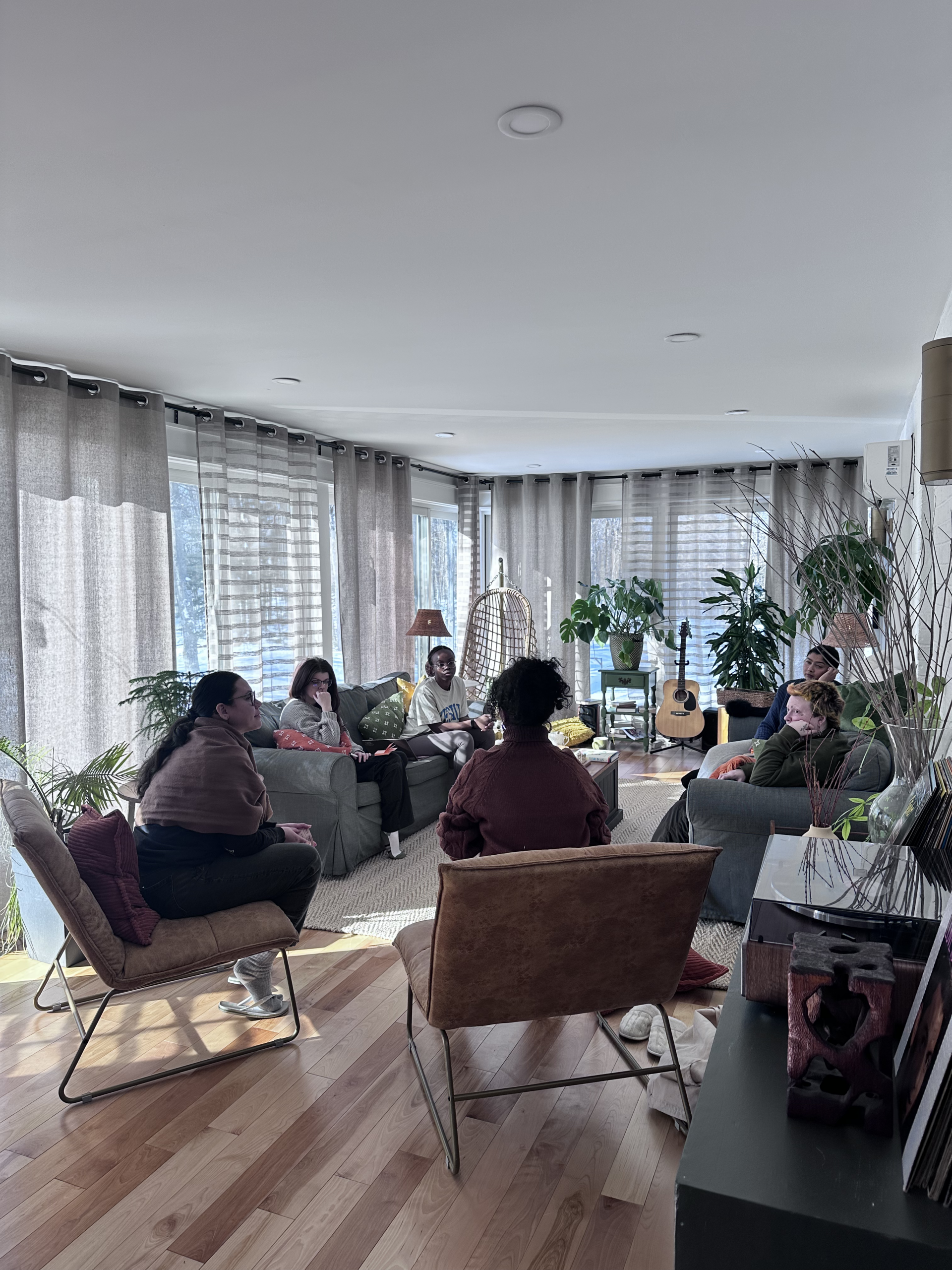 Photo of a group of young people engaged in conversation in a sunny living room space.
