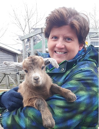 White woman wearing blue and green coat and holding a baby goat.
