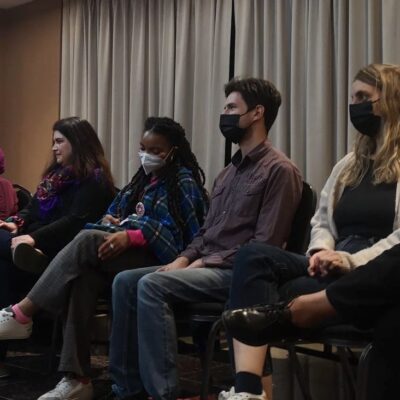 A group of people seated inside; some are wearing masks and some are not.